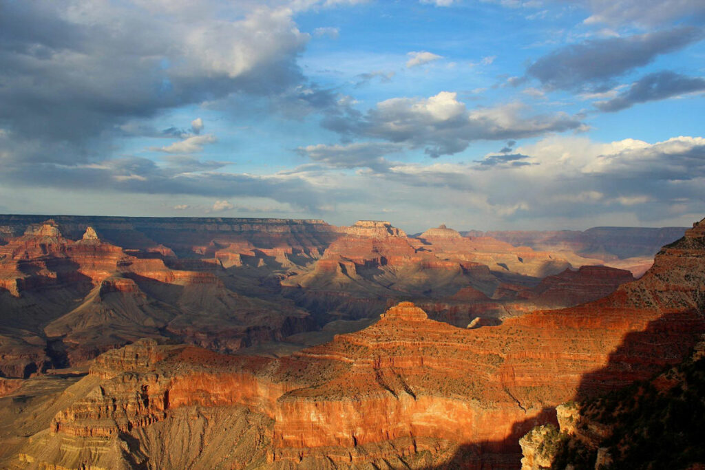 View spanning the across the Grand Canyon with sunlight highlighting the ridges and clouds.